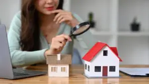 A woman looking at a model house through a magnifying glass.