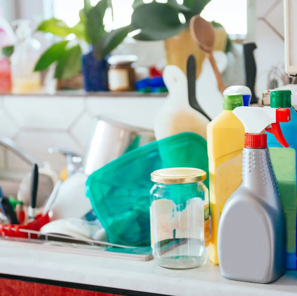 A counter top with cleaning supplies and dishes on it.