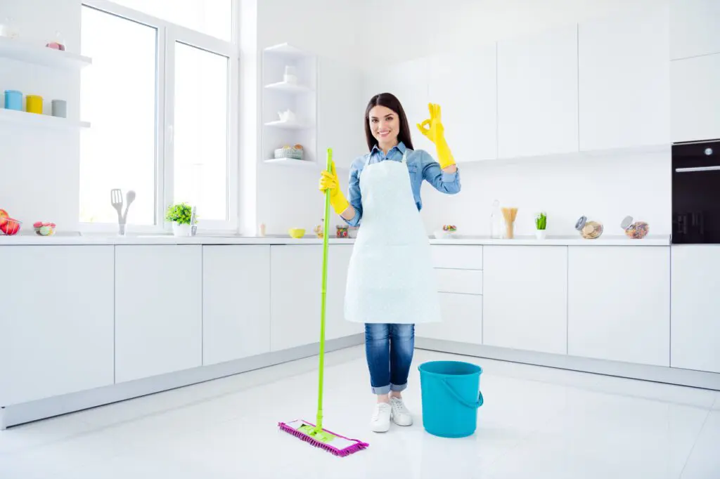 A woman in an apron and gloves is holding a mop.