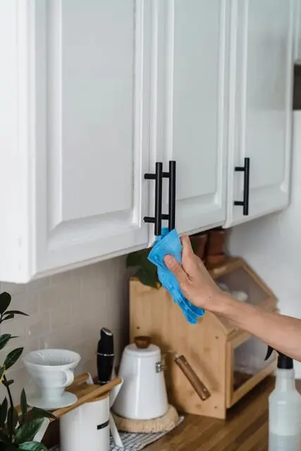 kitchen cleaning by wiping down the cabinets with a microfiber cloth