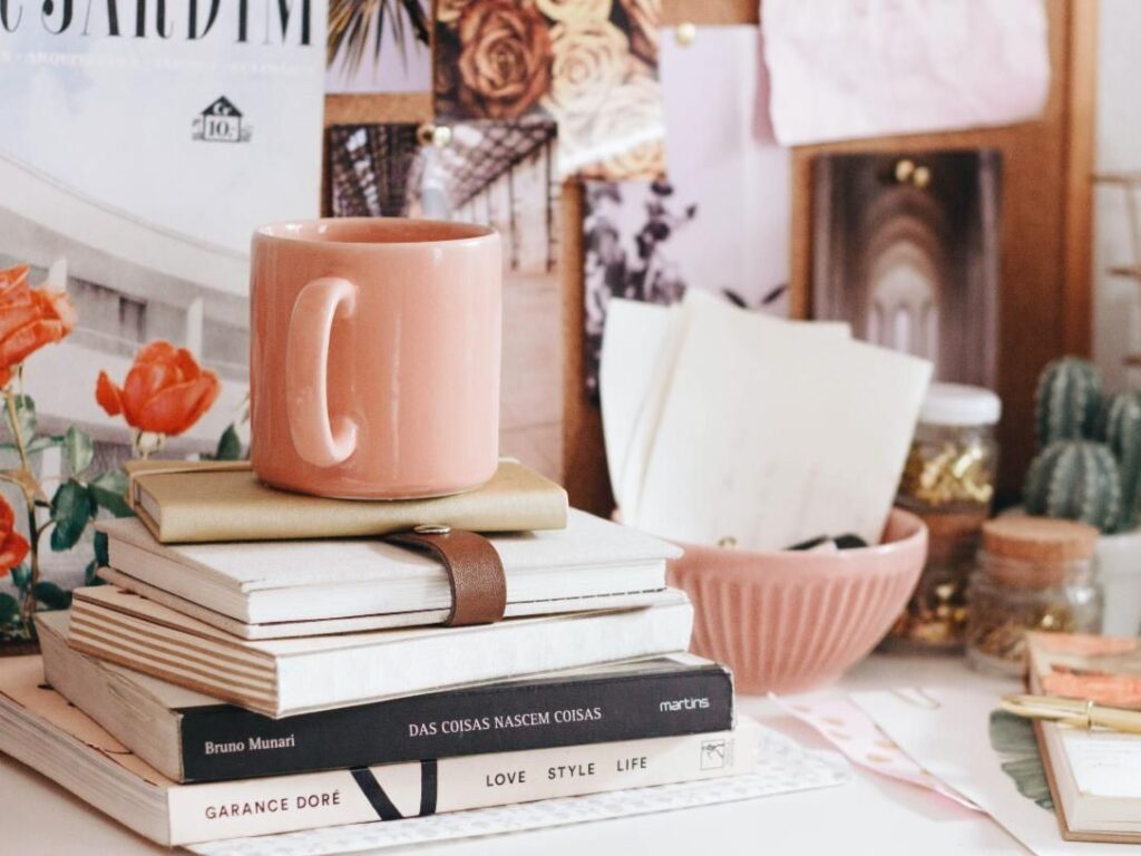 A cluttered desk with a stack of books, a mug, bowl, and random photos