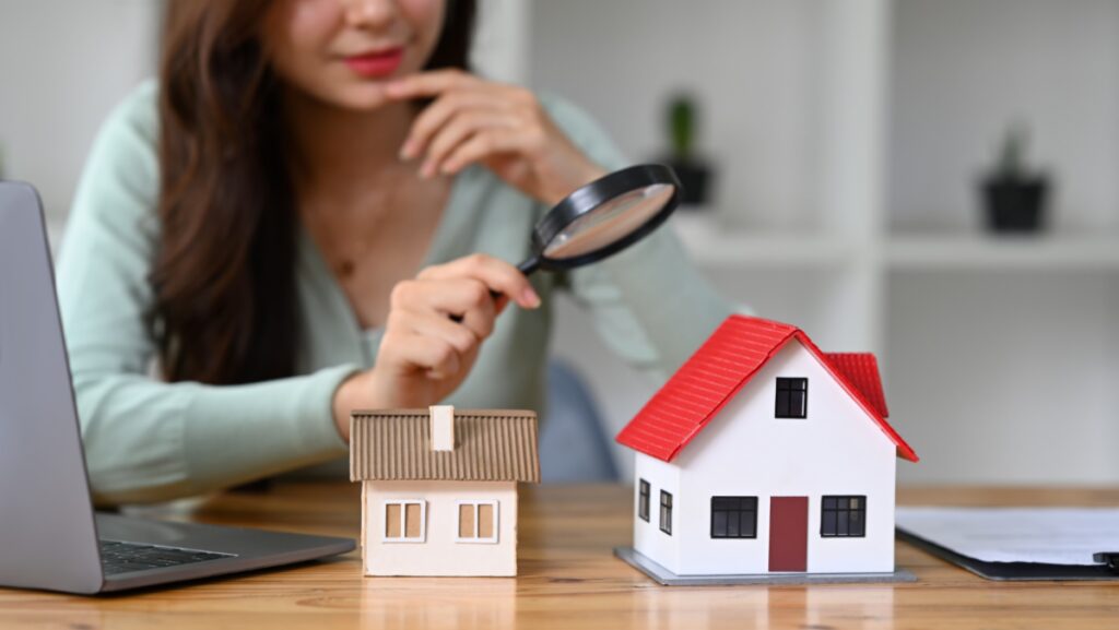 Focused woman with magnifying glass examining two small houses