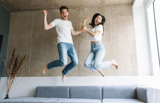 Joyful couple leaping off their couch in excitement, enjoying spring cleaning