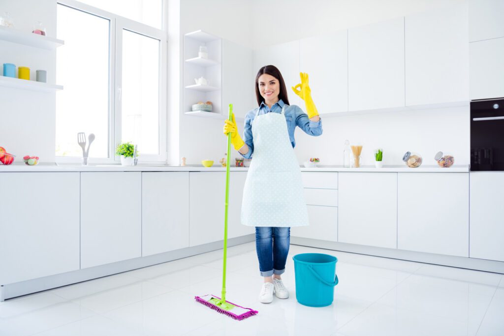 Woman in a spotless white kitchen, confidently holding a mop